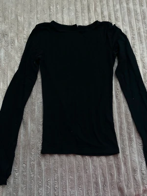 Svart långärmad topp - En enkel svart långärmad topp med rund hals. Modellen är figurnära och passar perfekt till både jeans och kjol. Tillverkad i mjukt material som känns skönt mot huden. Perfekt basplagg i garderoben.Är även öppen vid armarna.