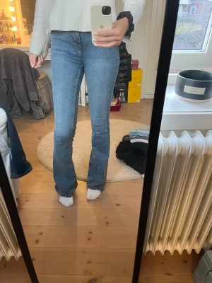 Blå bootcut jeans med hög midja - Snygga blåa bootcut jeans med hög midja och klassisk femficksdesign. Jeansen har en smal passform upptill och utsvängda ben nertill, vilket ger en trendig siluett. Perfekta för dig som gillar en avslappnad men ändå stilren look.