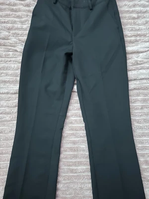 Svarta raka kostymbyxor - Snygga svarta kostymbyxor med raka ben och pressveck. Klassisk design med hällor för skärp och fickor fram. Perfekta till en stilren look och passar till många olika outfits.