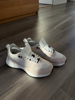 Dior b25 beige/ljusgrå - Snygga sneakers i vitt och beige från Dior med mesh- och mockadetaljer. Skorna har vita snören, svart detalj vid snörningen och en tjock vit sula. Perfekta för dig som gillar stilrena och moderna sneakers med sportig känsla.