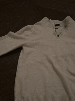 Ljusgrå halvzip tröja - Cashmere tröja med halvzip och hög krage. Tröjan har långa ärmar och ribbade muddar vid ärmslut och nederkant. Perfekt för en avslappnad och stilren look.