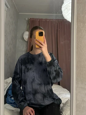 Svart och grå tie dye långärmad topp - Cool långärmad topp med svart och grå tie dye-mönster. Oversized passform med rund halsringning och muddar vid ärmsluten. Perfekt för en avslappnad och trendig look.