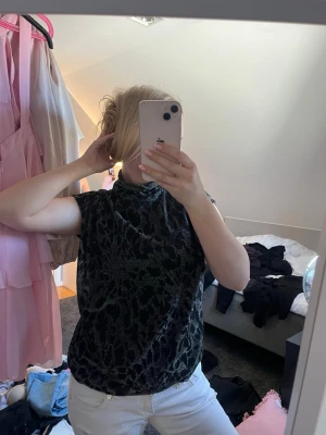 Svart glittrig leopardmönstrad topp - Säljer en svart glittrig topp med leopardmönster och hög hals. Toppen är ärmlös och har en loose passform som ger en avslappnad men ändå trendig look. Perfekt för dig som vill sticka ut lite extra.