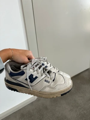 New Balance 550 vita och blå sneakers - Säljer ett par New Balance 550 sneakers i vitt och marinblått. Skorna har klassisk låg siluett, perforerade detaljer på sidorna och tydlig logga. Ovandelen är i läder och sulan är robust med bra grepp. Perfekta för dig som gillar retrostil och streetwear.