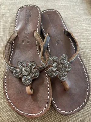 Bruna sandaler med pärlblommor - Helt Nya! Säljer ett par bruna sandaler från British London.