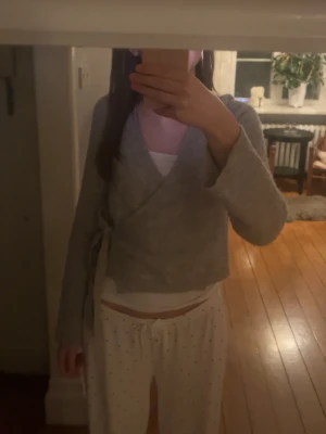 Grå omlottkofta med knytband - Mysig grå omlottkofta med långa ärmar och knytband i sidan. Koftan har en enkel och stilren design, perfekt att slänga över ett linne eller t-shirt. Materialet ser mjukt och bekvämt ut, och modellen är något kortare i midjan. Använt bara ett få tal gånger