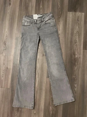 Grå bootcut jeans  - Säljer ett par grå bootcut jeans från lager 157 med broderade detaljer på bakfickorna. Jeansen har klassisk femficksmodell, normal midja och utsvängda ben. Tillverkade i denim med en mjuk tvättad look. Perfekta för en avslappnad och trendig stil.