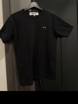 Svart t-shirt Comme des Garçons Play - Svart t-shirt från Comme des Garçons Play med det ikoniska hjärta med ögon broderat på bröstet. Klassisk rund hals och korta ärmar. Tillverkad i mjuk bomull för skön känsla och stilren look.