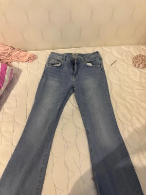 Ljusblå bootcut jeans - Säljer ett par ljusblå bootcut jeans med klassisk femficksdesign och normal midja. Jeansen har en snygg tvätt och är tillverkade i mjukt denimtyg. Perfekta för en avslappnad och trendig look.