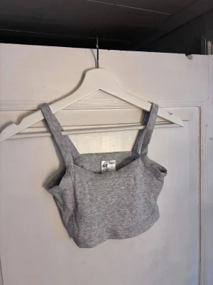 Ljusgrå ribbad topp H&M för barn - Säljer en ljusgrå ribbad topp från H&M som är till för barn. Toppen är croppad och har en enkel, stilren design. Tillverkad i mjuk bomullsmix för skön känsla hela dagen. Helt ny med prislapp.