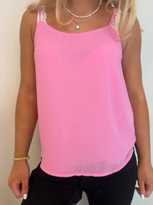 Rosa linnetopp med spetsdetalj - Snygg rosa linnetopp med tunna axelband och vit spetsdetalj vid axlarna. Perfekt för varma dagar och enkel att styla med olika outfits. Luftigt material som känns skönt mot huden.