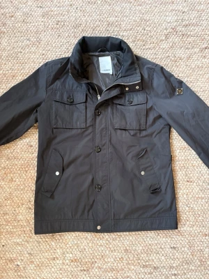 J.Lindeberg Bailey field jacket  - Säljer denna riktigt feta J.Lindeberg field jacketen⭐️Det är en tunn jacka som passar perfekt nu på våren🌟. Storlek L men passar även M👍, Nypris=4000kr!🤝. Skick:9/10, den enda defekten som finns är ett litet vitt streck vid den vänstra magfickan, men som bara syns om man kollar riktigt nära🙌. Hör gärna av er vid frågor eller funderingar 