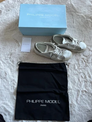 Philippe Model sneakers i läder - Snygga vita sneakers från Philippe Model Paris med grå detaljer och klassisk låg siluett. Skorna är tillverkade i läder med mockadetaljer och har en ikonisk logotyp på sidan. Perfekta för en trendig och avslappnad stil.