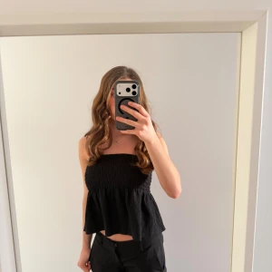 Svart tubtopp med volang - En svart bandu topp med volang och ribbat matrial.   Tjocktlager vid brösten så bh behövs eventuellt inte!