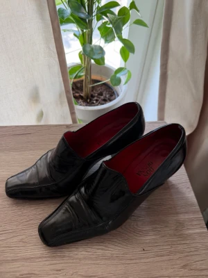 Högklack Loafers i äkta läder  - Stilrena svarta loafers från Don Donna med glansig finish och fyrkantig tå. Skorna har en unik röd insida som ger en cool kontrast. Äkta läder.