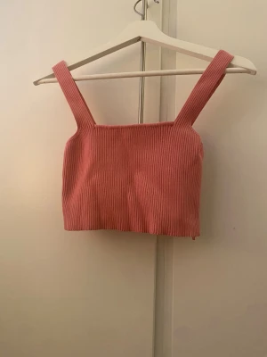 Rosa ribbad croppad strechy topp - Säljer en söt rosa croppad strechy topp med breda axelband och ribbad struktur. Perfekt för varma dagar och enkel att styla med jeans eller kjol. Toppen är ärmlös och har en mjuk, stretchig känsla.passar även small.