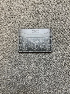 Svart kortfodral från Goyard - Snyggt svart kortfodral från Goyard med klassiskt mönster i vitt och grått. Fodralet har flera kortfack på både fram- och baksidan och är tillverkat i läder med canvasdetaljer. Perfekt för dig som vill ha en stilren och exklusiv accessoar.