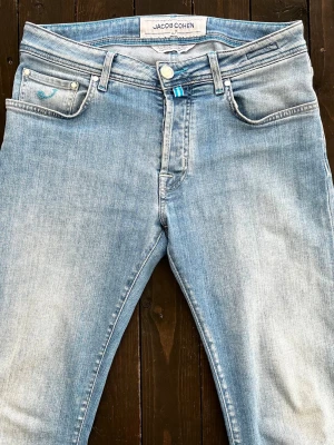 :Jacob Cohën ljusblå jeans W32/L32 – Mycket fint skick -  Stilrena ljusblå jeans från Jacob Cohën i mjukt och stretchigt material som ger en mycket bekväm passform. Exklusiva detaljer med blå kontrastsömmar, signaturknappar och märkets karakteristiska detaljer på ficka och bakre etikett. Perfekta för både vardag och en mer uppklädd