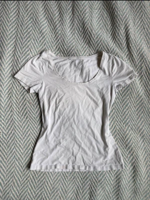 Vit basic t-shirt med rund hals - En enkel vit t-shirt med rundad halsringning och korta ärmar. Modellen är figurnära och passar perfekt till alla typer av outfits. Tillverkad i mjuk bomull för skön känsla hela dagen.