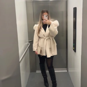 Beige kappa från DM Design - Superfin beige kappa från DM Design med stor huva kantad av fluffig äkta päls. Knyts i midjan med bälte för snygg siluett. Långärmad och i mjukt material som känns lyxigt. Passar storlek S och M