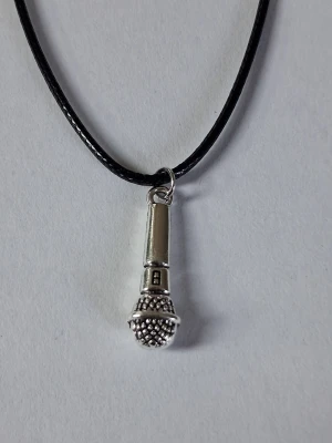 Halsband med mikrofonhänge - Snyggt vaxat läderhalsband med ett silverfärgat mikrofonhänge i metall. Hänget har detaljerad design och hänger på ett svart, tunt läderhalsband.