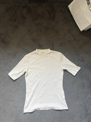Vit ribbad polotopp Carin Wester - Vit ribbad polotopp från Carin Wester i storlek M. Toppen har korta ärmar och en högre krage som ger en clean och stilren look. Perfekt att styla med jeans eller kjol för en enkel men snygg outfit. Har två sminkfläckae på framsidan.