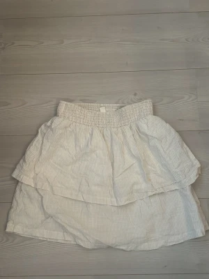 Vit kortkjol med volang  - Söt vit kortkjol i ljusbeige / vit färg. OBS: har en liten fläck, annars i bra skick! Inga shorts under kjolen, midjan är stretchig. Storlek S, men passform XS-M 