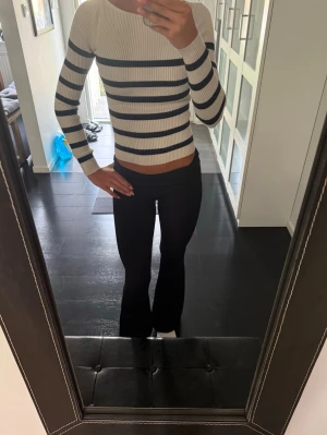 Randig ribbstickad tröja  - Säljer en snygg ribbstickad tröja som är skön och fin. Tröjan är beige med mörkblåa horisontella ränder och har lång ärm. Figurnära passform och stretchigt material som ger en modern look.