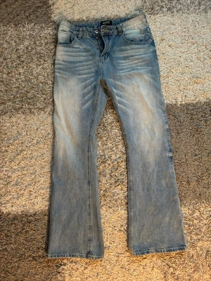 Ljusblå bootcut jeans med slitningar - Säljer ett par ljusblå bootcut jeans, tydliga slitningar framtill och baktill. Jeansen har klassisk femficksmodell, normal midja och dragkedja med knapp. Materialet är denim i bomull och de har en avslappnad vintage-look. Finns ett hål som skulle behövas sy igen som ni ser på sista bilden