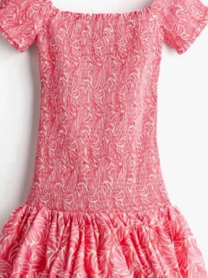 Rosa kortklänning med volang - Söt rosa kortklänning med mönster i vitt och smockad överdel. Klänningen har korta ärmar och en volangig kjol som ger en lekfull look. Perfekt för varma dagar och somriga tillfällen.💓