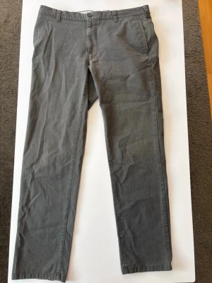 Grå chinos med raka ben - Snygga grå chinos med klassisk rak passform och bälteshällor. Byxorna har sidofickor fram och två passpoalfickor bak. Tillverkade i ett mjukt bomullstyg som ger en avslappnad men stilren look. Perfekta för dig som gillar enkel och clean stil.