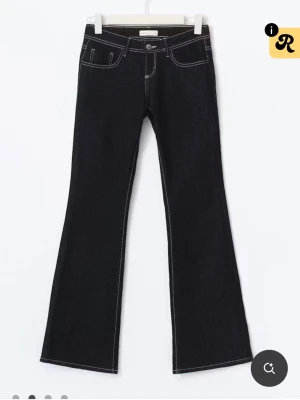 Svarta bootcut jeans med kontrastsömmar - Snygga mörkblå bootcut jeans med vita kontrastsömmar och klassisk femficksmodell. Jeansen har låg midja och är bootcut. Lite slitna nertill i bak men inget man tänker på💕