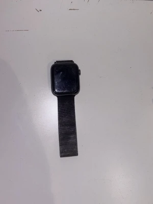 Svart smartklocka med mesh-armband - Stilren svart smartklocka med rektangulär urtavla och magnetiskt mesh-armband i metall. Klockan har en knapp på sidan och en slimmad design som passar till de flesta stilar. Perfekt för dig som vill ha koll på notiser och hälsa direkt på handleden.