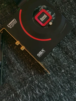 Sound Blaster SBX ljudkort PCIe - Säljer ett svart Sound Blaster SBX ljudkort med röda detaljer och hexagonmönster. Kortet ansluts via PCIe och har guldpläterade kontakter. Perfekt för dig som vill uppgradera ljudet i din dator och få bättre ljudupplevelse vid gaming eller musik.