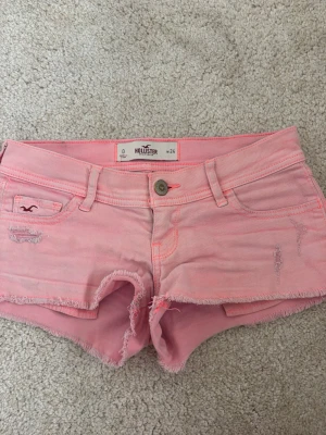 Rosa jeansshorts från Hollister - Säljer ett par ljusrosa jeansshorts från Hollister med fransig kant och slitna detaljer. Shortsen har klassisk femficksdesign, bälteshällor och knappgylf. Perfekta för varma dagar och ger en avslappnad vibe.💓