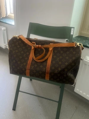 Louis Vuitton Monogram weekendbag - Snygg och klassisk weekendbag från Louis Vuitton i brunt monogrammönster med detaljer i ljust brunt läder. Väskan har både handtag och axelrem i läder samt guldfärgade metalldetaljer. Perfekt för resor när du vill resa med stil.