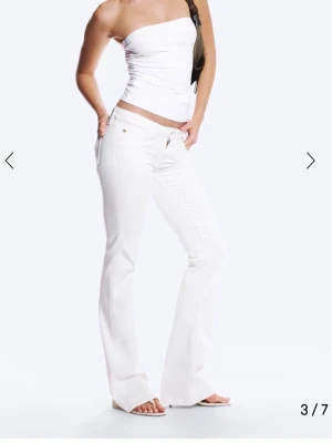 Vita bootcut jeans med hög midja - Säljer ett par vita bootcut jeans med hög midja och klassiska fem fickor. Jeansen har en snygg passform som framhäver benen och en liten patchdetalj bak på linningen. Perfekta för dig som vill ha en clean och fräsch look. (Oanvända) storlek 26/32