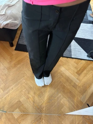 Svarta raka kostymbyxor - Snygga svarta kostymbyxor med hög midja och raka ben. Byxorna har pressveck framtill och stängs med knapp och dragkedja. Perfekta till en stilren look och passar till många olika outfits.
