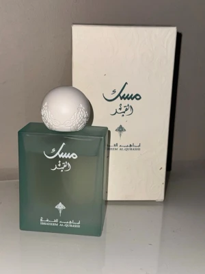 Parfym Ibraheem Al-Qurashi grön - Snygg parfymflaska från Ibraheem Al-Qurashi i frostat grönt glas med vit dekorativ rund kork. Flaskan har arabiska bokstäver och kommer med en matchande vit kartong med mönster. Perfekt för dig som gillar exklusiva dofter och stilren design.