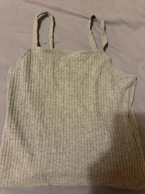 Grå ribbad linnetopp - Säljer en enkel och stilren grå linnetopp med smala axelband. Toppen är ribbad och har en rak passform, perfekt att matcha med jeans eller kjol. Materialet känns mjukt och stretchigt, vilket gör den bekväm att bära.