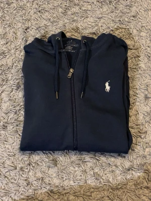 Ralph Lauren hoodie - Tjena! Säljer en blå zip hoodie från Ralph lauren. Den är givetvis äkta. Ända nackdelen är att dragkedjan är lite sliten (sista bilden) men den fungerar ändå och är inget man tänker på när man har den på sig. Skriv vid frågor eller intresse!:) 