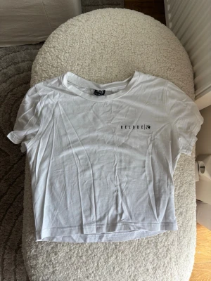 Vit croppad t-shirt från Relode - Säljer en vit croppad t-shirt från Relode med enkel svart logga på bröstet. T-shirten har korta ärmar och är gjord i mjuk bomull, perfekt till jeans eller shorts. Enkel och clean stil som passar till det mesta.