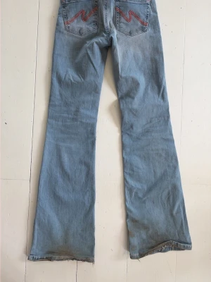 Ljusblå bootcut jeans från Nelly - Säljer ett par ljusblå bootcut jeans från Nelly med röda sömmar på bakfickorna och råa kanter nedtill. Jeansen har klassisk femficksdesign och knappgylf. Perfekta för en avslappnad och trendig look.