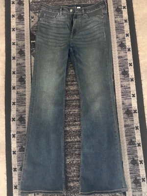 Blå bootcut jeans med utsvängda ben - Snygga blå bootcut jeans med klassisk femficksdesign och utsvängda ben. Jeansen har en lätt tvättad look och normal midja. Perfekta för dig som gillar retrostil och vill ha ett par jeans som sticker ut lite extra.