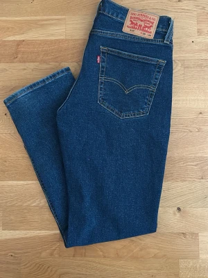 Levi's 514 raka blå jeans W30 L30 - Klassiska blå jeans från Levi's modell 514 med rak passform. Jeansen har fem fickor, tydliga kontrastsömmar och Levi's ikoniska läderpatch bak i midjan. Tillverkade i slitstark denim med en djupblå tvätt och röd Levi's-tag på bakfickan.