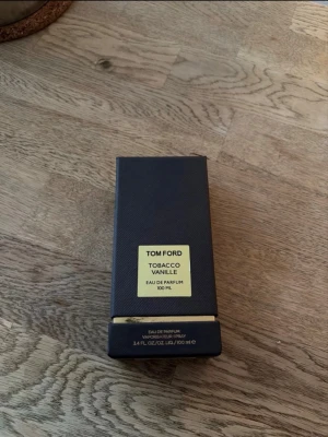 Tom Ford Tobacco Vanille 100 ml parfym - Tom Ford Tobacco Vanille Eau de Parfum i en lyxig mörkblå kartong med guldfärgad etikett. Parfymen har en elegant och stilren förpackning och är känd för sin rika doft av tobak och vanilj. Perfekt för dig som gillar exklusiva dofter.