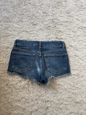 Mörkblå jeansshorts med fransig kant - Snygga mörkblå jeansshorts med fransig kant. Perfekta för varma dagar och enkel att matcha med olika toppar. Använda fåtal gånger och säljer då de inte kommer till användning 