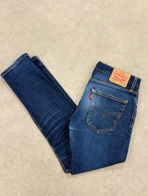 Levi's 512 blå / mörkblå jeans W31 L32 - Säljer ett par klassiska blå Levi's 512 jeans med smal passform och snygg tvätt. Jeansen har fem fickor, gul kontrastsöm och den ikoniska läderlappen bak i midjan. Perfekta för en avslappnad och trendig look.  #grisch #stockholm #archive