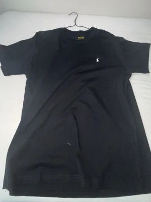 Svart t-shirt från Polo Ralph Lauren - Klassisk svart t-shirt från Polo Ralph Lauren med liten vit logga broderad på bröstet. T-shirten har rund halsringning och korta ärmar. Tillverkad i mjuk bomull för en skön känsla och enkel stil.