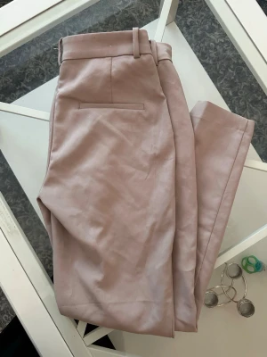 Beige kostymbyxa från H&M - Säljer ett par stilrena beige kostymbyxor från H&M i storlek 40. Byxorna har hög midja, raka ben och en diskret bakficka. Materialet är mjukt och har en lätt stretch för extra komfort. Perfekta för en clean och modern look.